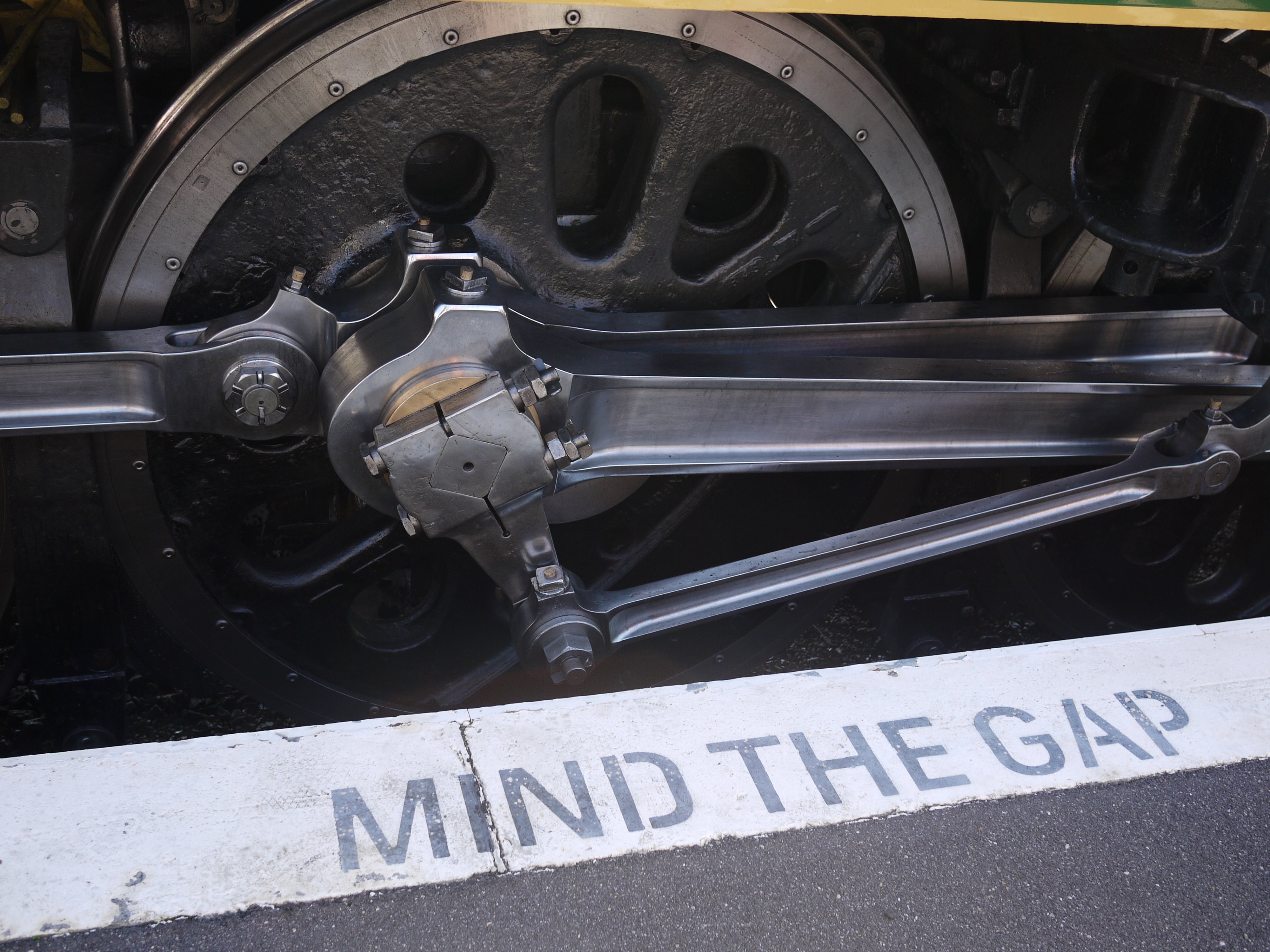 The wheels of a steam locomotive by the station platform with Mind the Gap visible on the platform