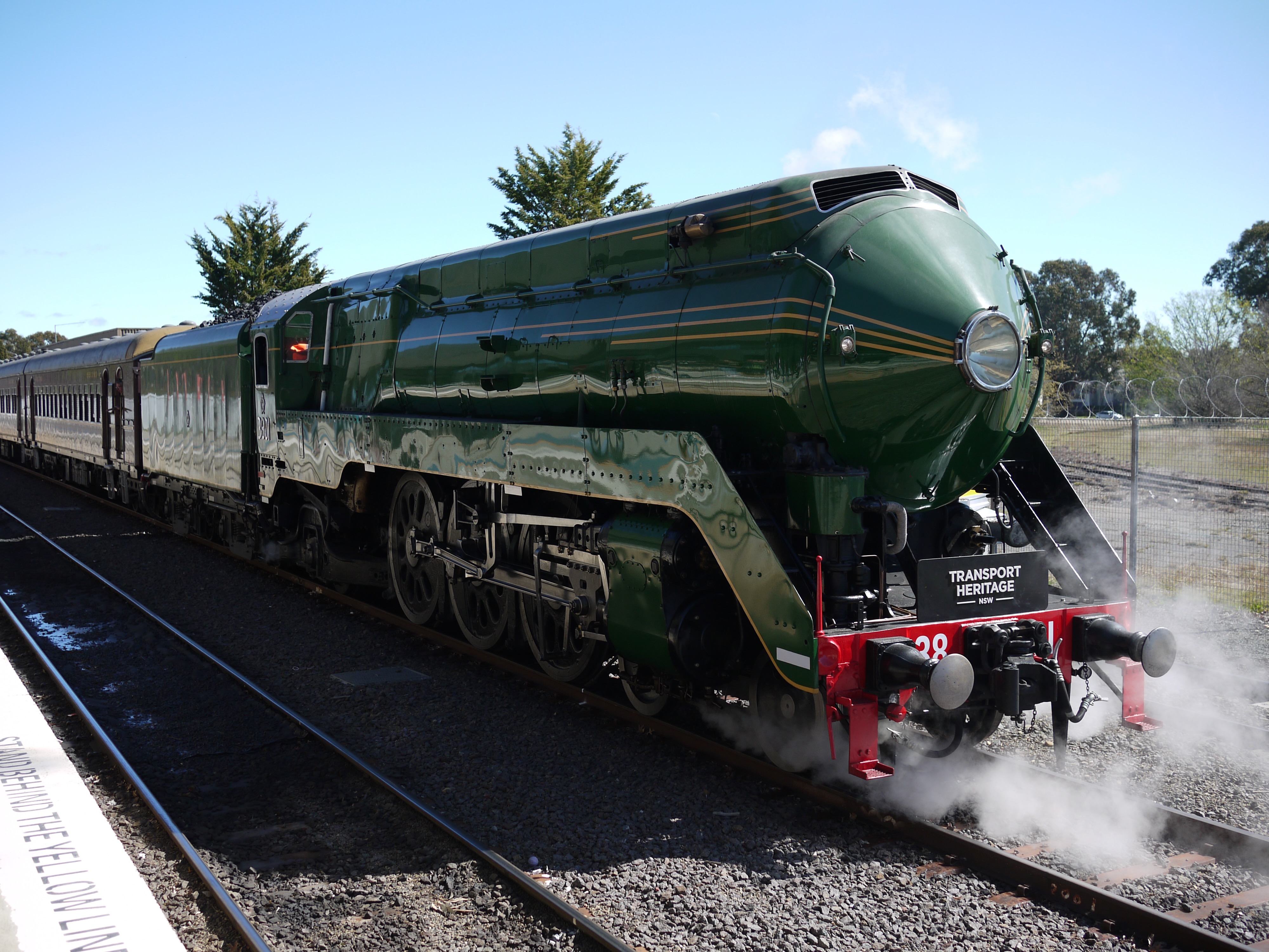 A green steam locomotive next to a chain-link fence